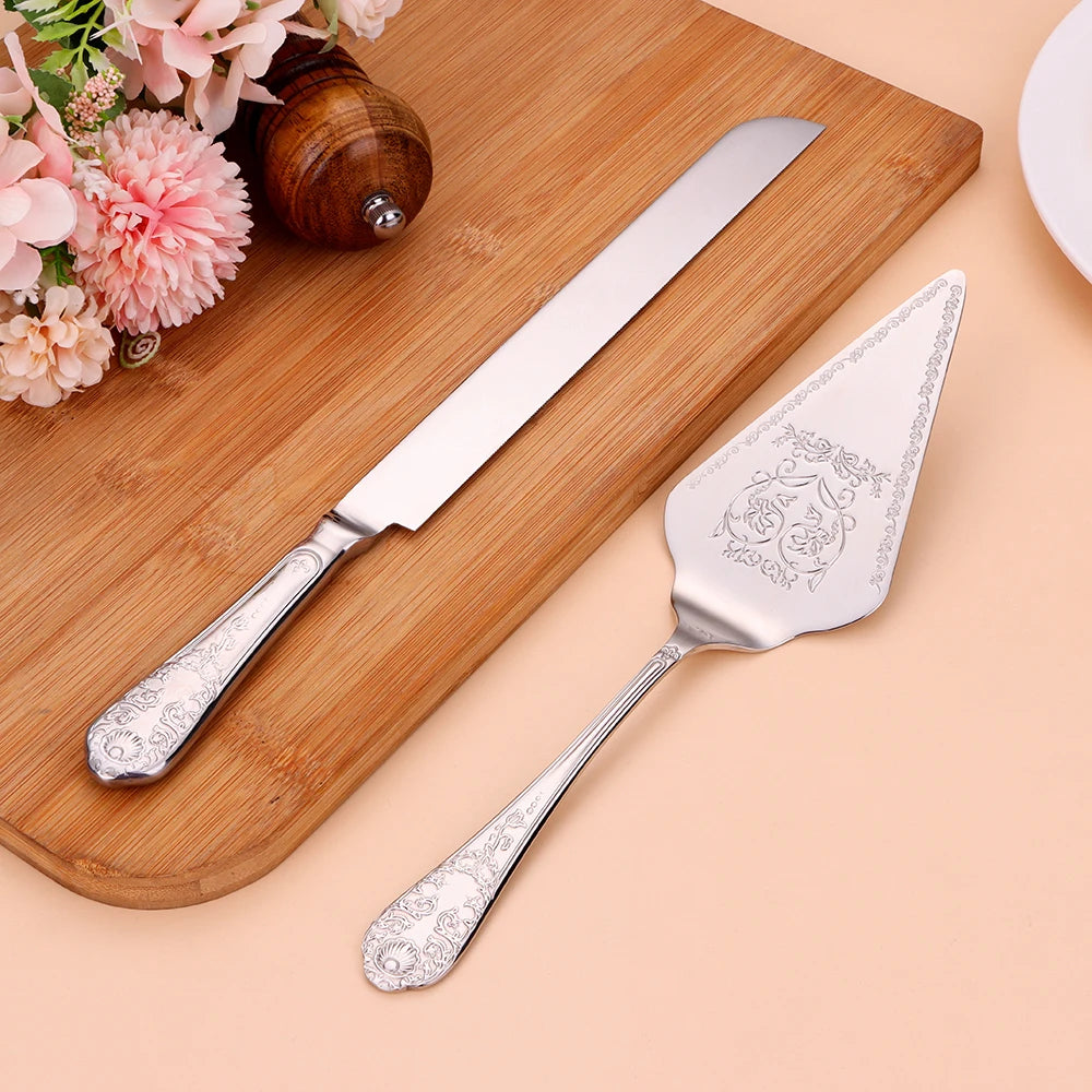 Silver cake knife and server set on a wooden board with flowers in the background