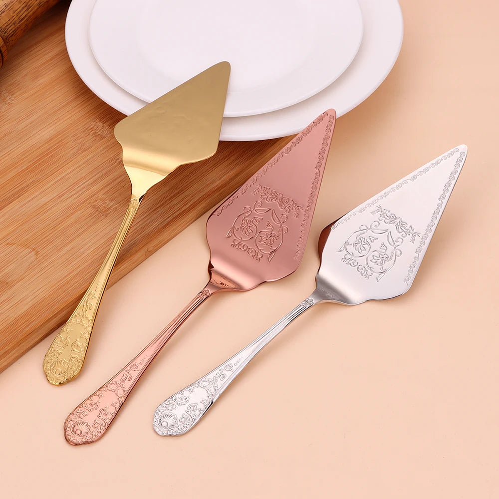 Three cake knives in gold, rose gold, and silver on a wooden surface.