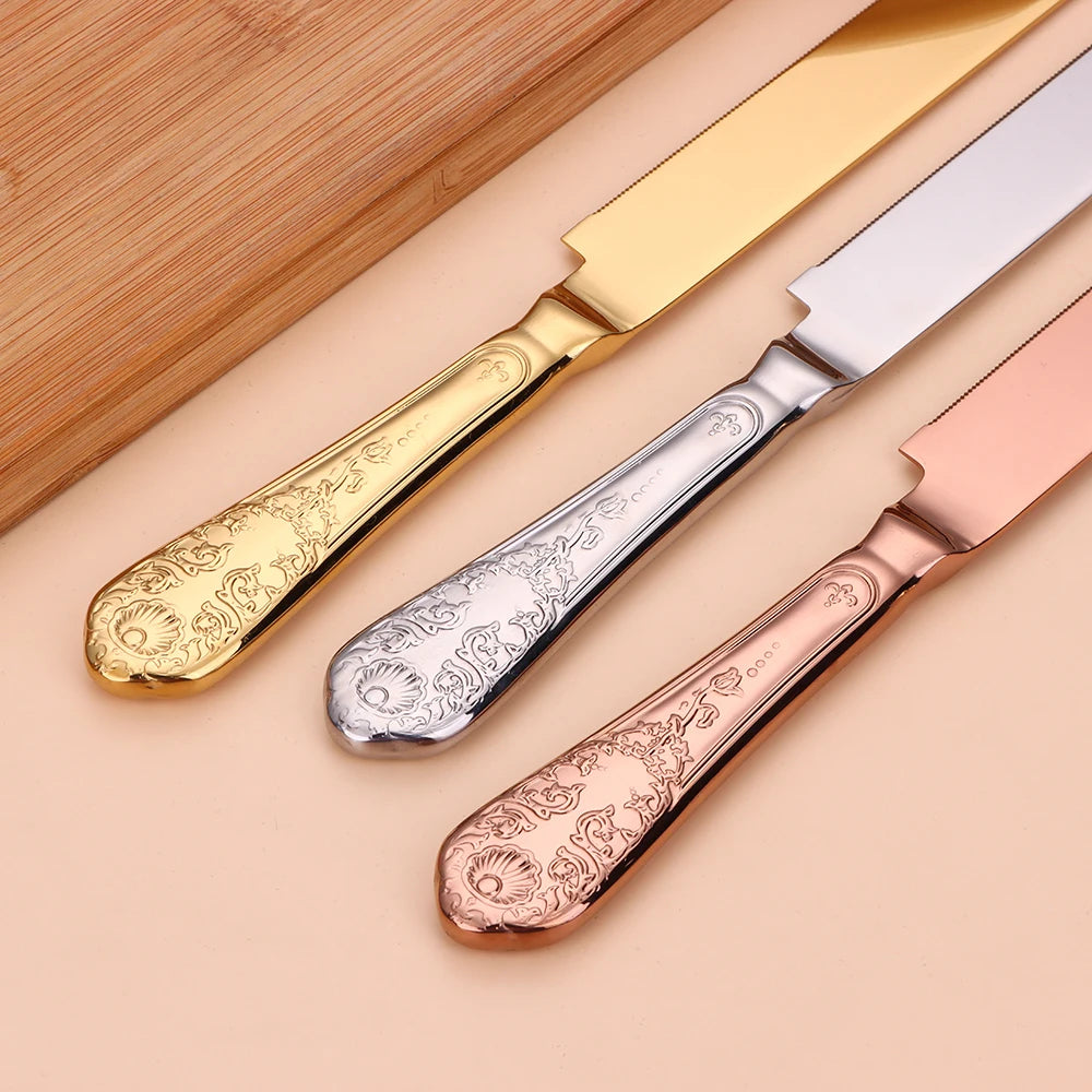 Three ornate butter knives in gold, silver, and rose gold on a beige background.