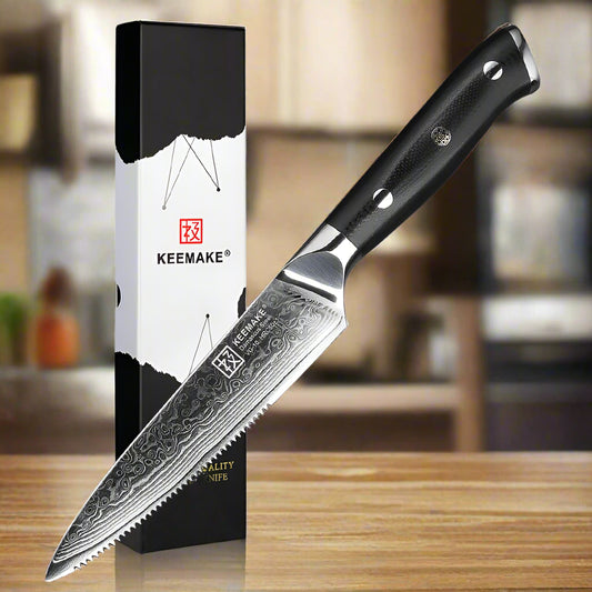 Serrated knife with black handle and detailed blade next to its packaging on a white background