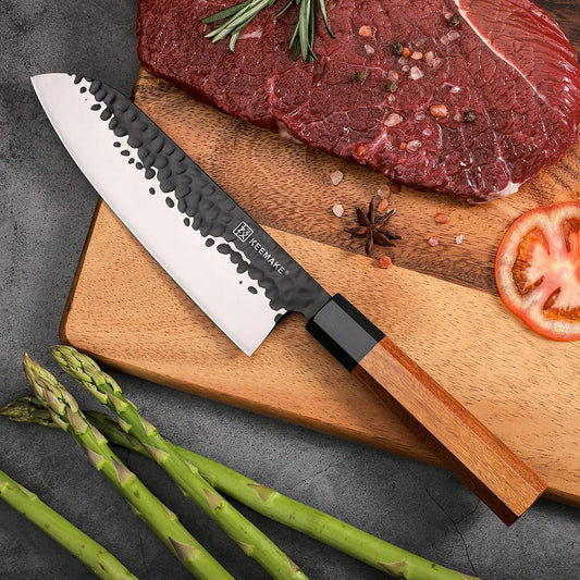 Chef's knife on a wooden cutting board with raw meat, asparagus, and tomatoes.