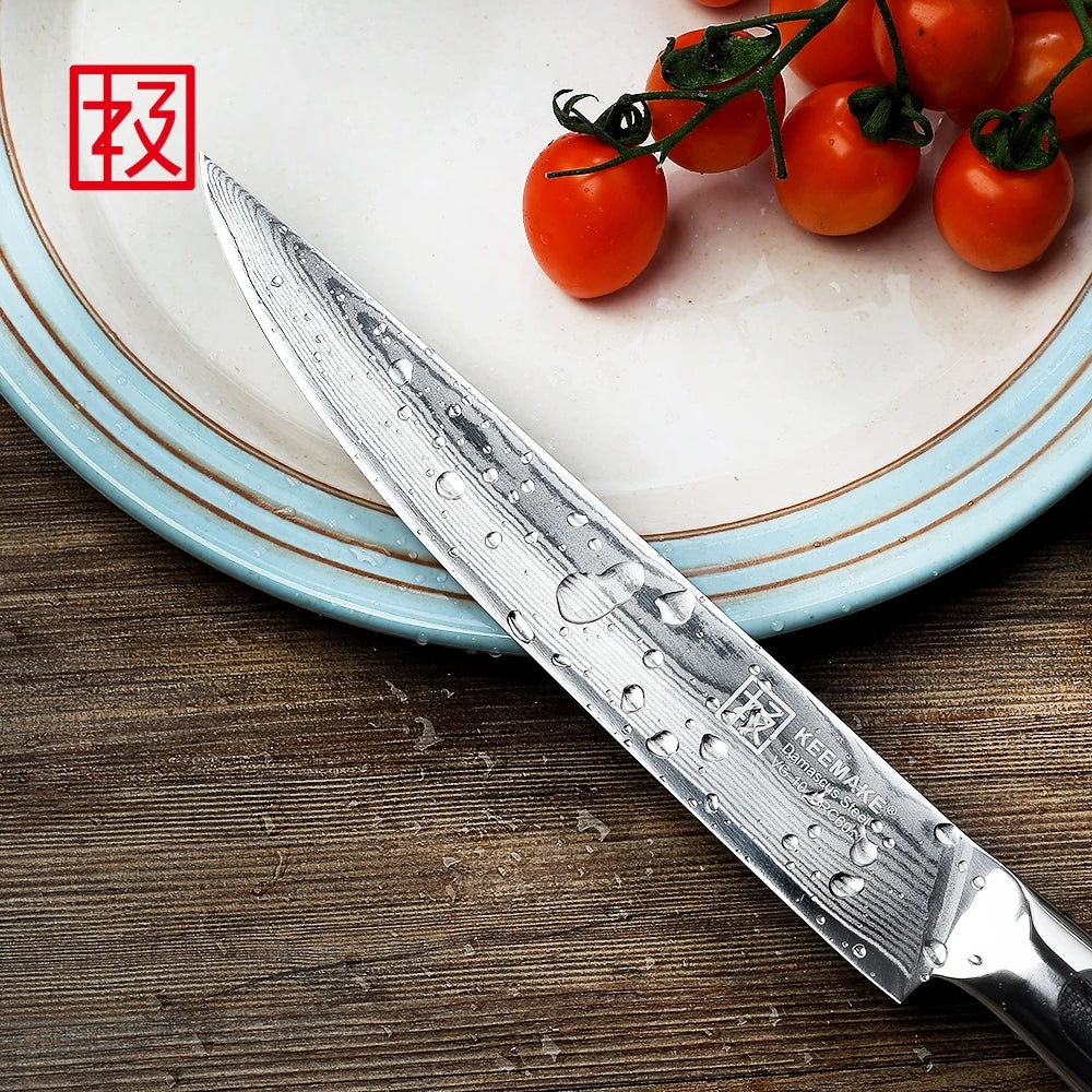 Knife with water droplets on a wooden surface next to cherry tomatoes on a plate.