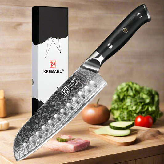Keemake chef's knife with black handle and detailed blade design, next to its packaging on a white background.
