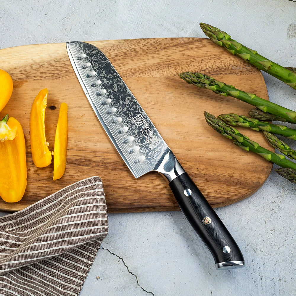 Chef's knife on a wooden cutting board with vegetables on a light gray surface