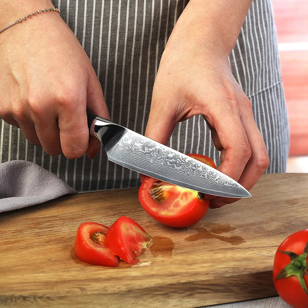 Person cutting a tomato with a Damascus steel knife on a wooden cutting board.