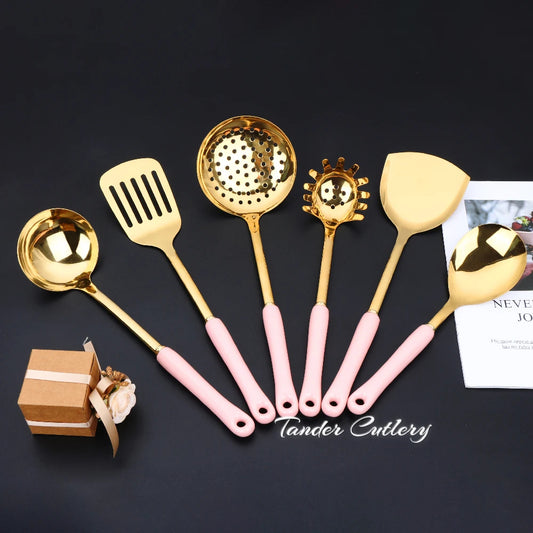 Set of gold kitchen utensils with pink handles on a dark surface, featuring the brand 'Tender Cutlery'.