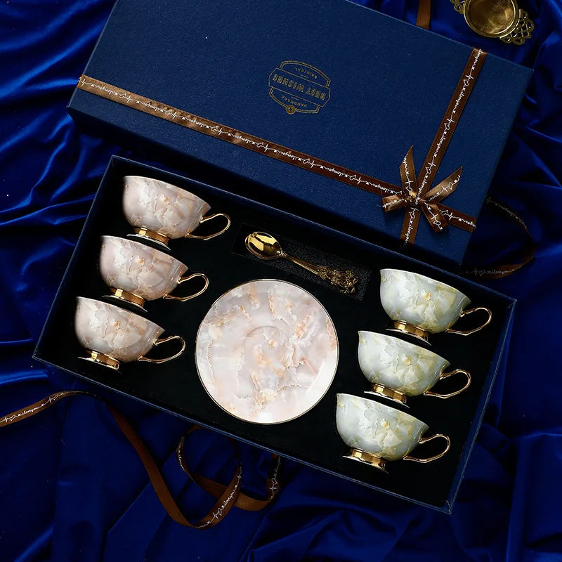 Set of marble-patterned tea cups and saucers with gold accents in a decorative box on a blue satin background.