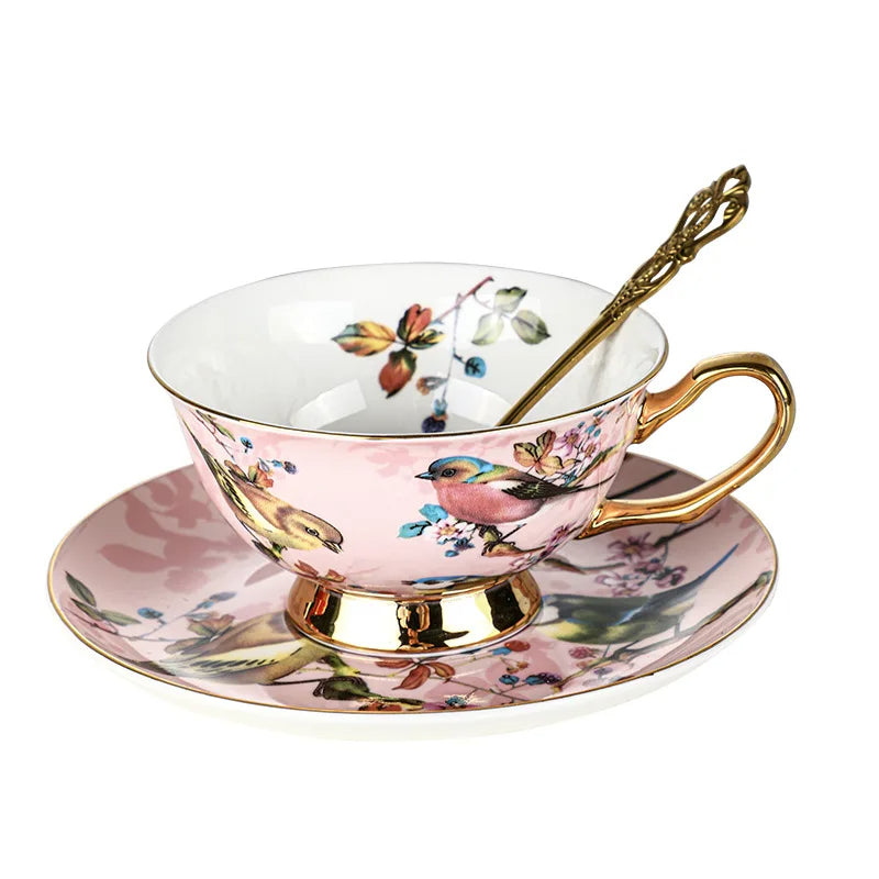 Teacup with floral and bird design on a matching saucer, featuring a gold handle and spoon.