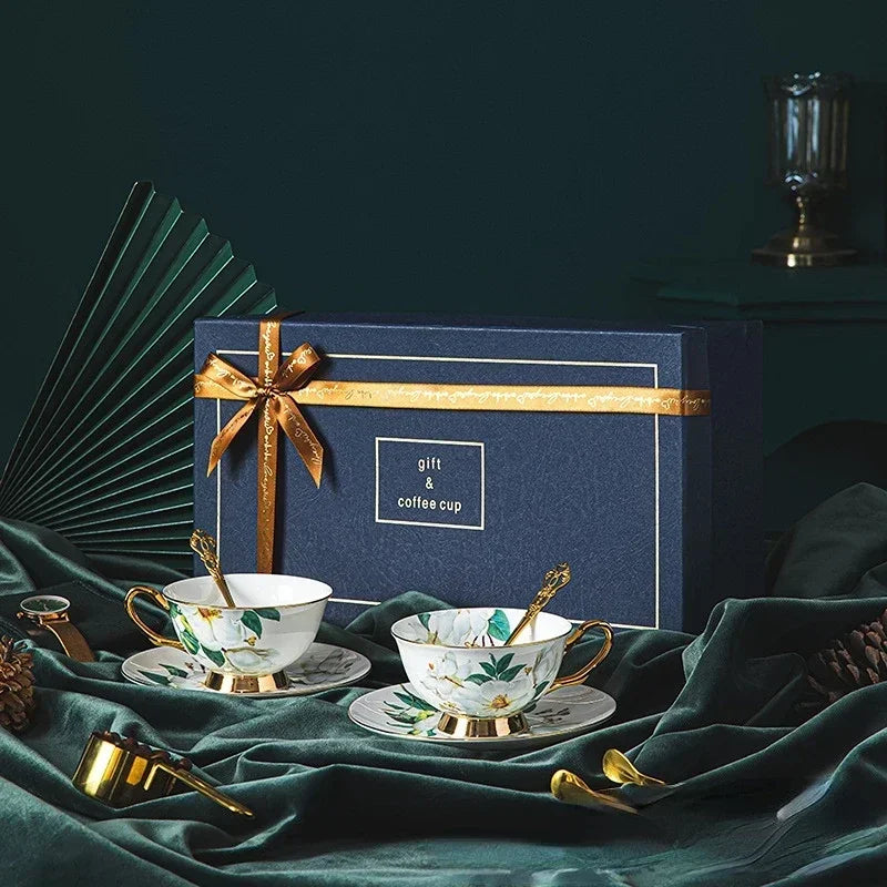 Gift set with two coffee cups, saucers, and spoons on a dark green fabric background.