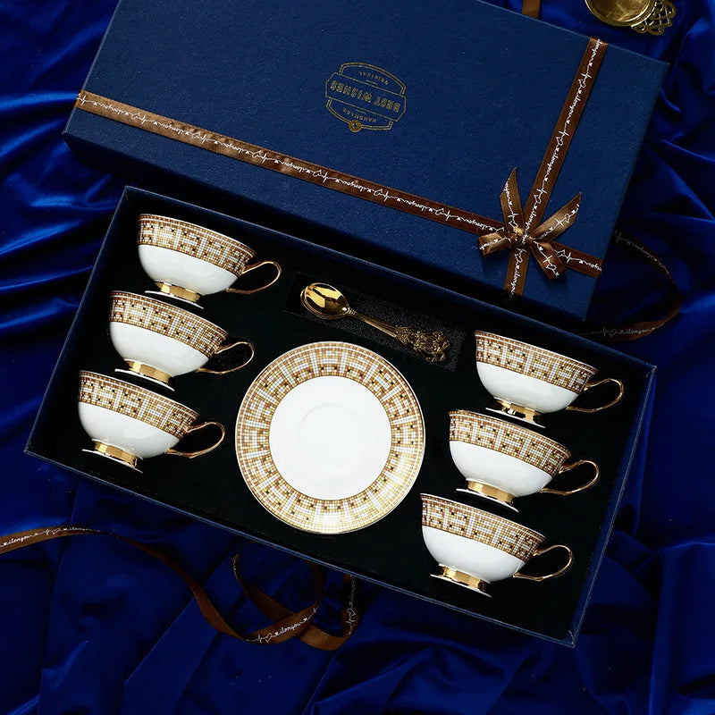 Set of white and gold ceramic tea cups and saucers in a decorative box on a blue satin background.