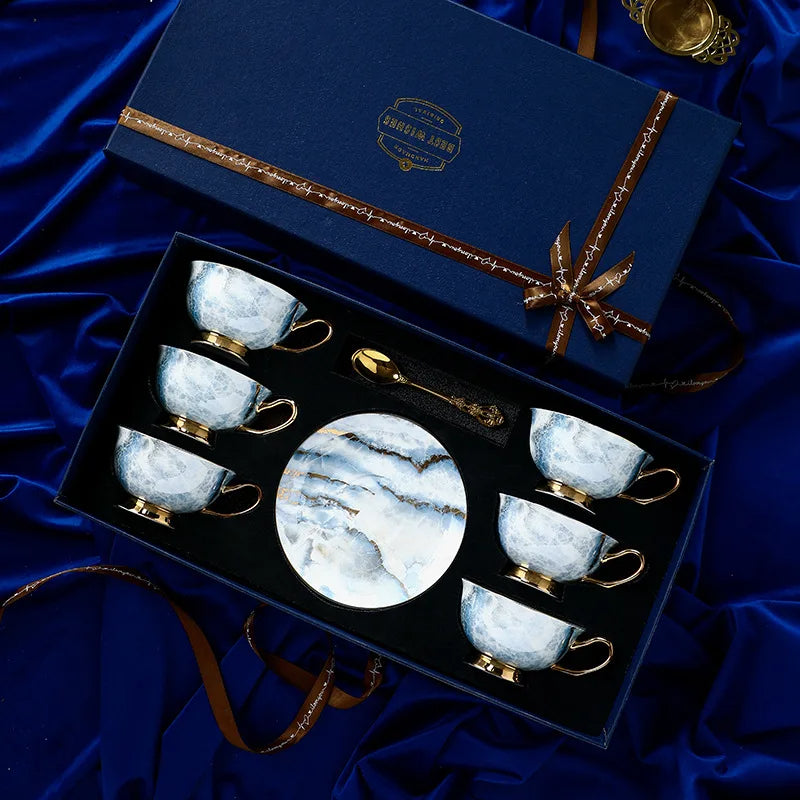 Set of marble-patterned tea cups and saucers in a decorative box on a blue fabric background.