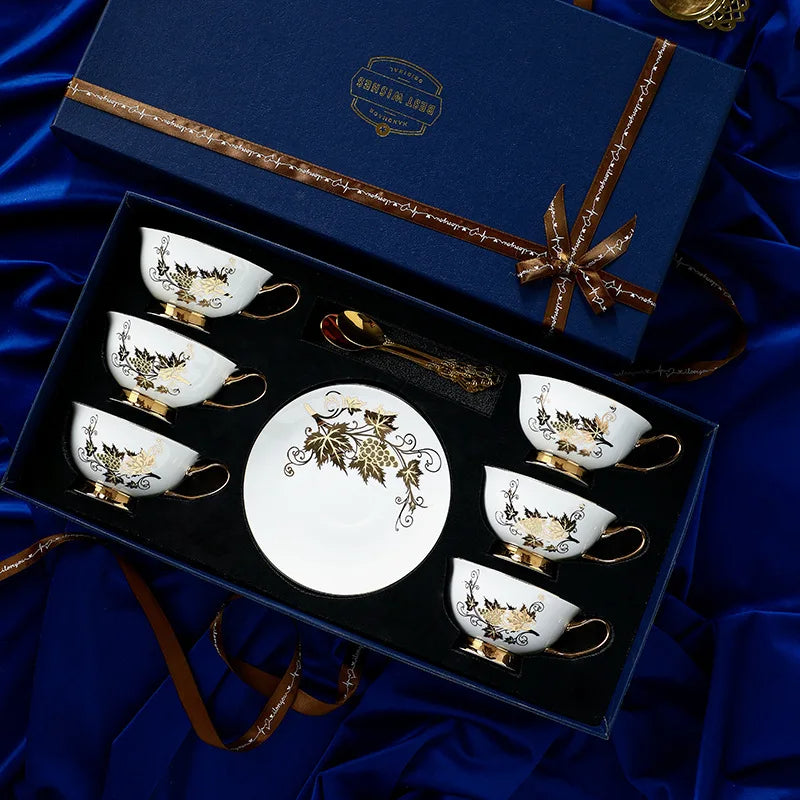 Set of decorative tea cups and saucers with a central plate in a gift box on a blue fabric background.