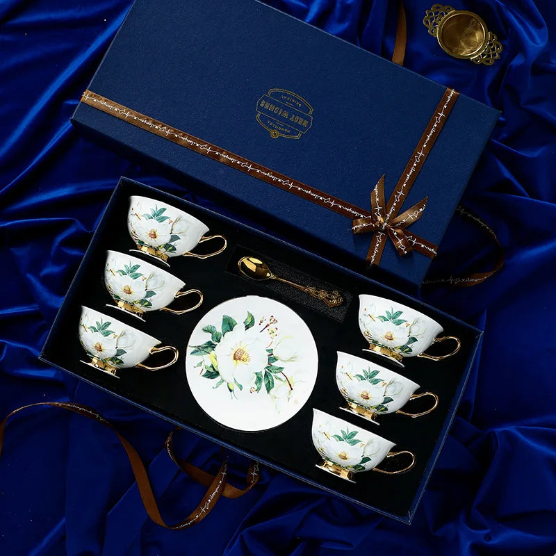 Set of ceramic tea cups and saucers with floral design in a decorative box on blue fabric.